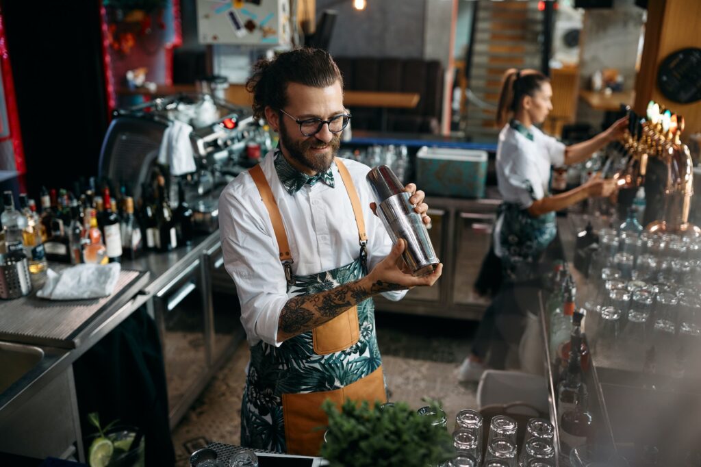 Happy barista making a cocktail while working at bar counter.