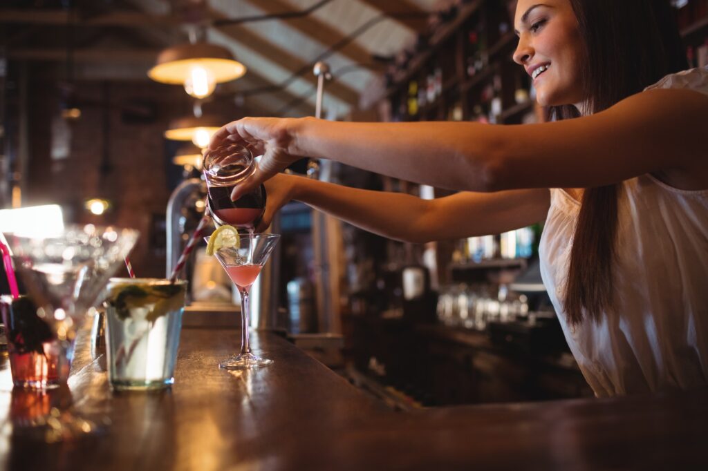 Pretty bartender pouring a cocktail drink in the glass